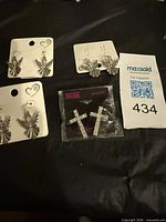 Overview of three angel earring pairs and one packaged cross earring pair