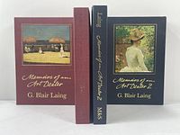 Front view of two volumes of Memoirs of an Art Dealer by G. Blair Laing with matching colored slipcases, showing illustrated covers and gold embossed titles.