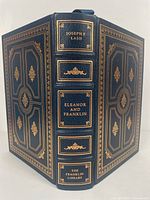 Photo of book front and back cover showing dark blue leather binding with gold gilt embossing and title on spine.