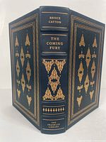Photo of the book cover showing dark blue full leather binding with detailed gold gilt designs on front, back and spine. The spine reads Bruce Catton, The Coming Fury, The Franklin Library.