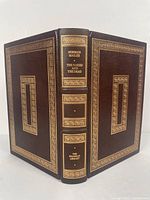 Full view of the leather bound book showing front, spine and back cover with gold gilt decoration and text.