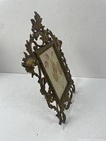 Side view of ornate gilt cast iron frame standing on its easel leg with visible photo insert of floral art.
