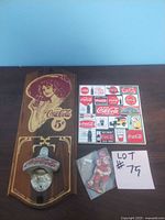 Wooden Coca-Cola wall plaque with vintage woman design and metal bottle opener, decorative tile with various classic Coca-Cola ads, and Santa Claus fridge magnet shown together on a wooden surface.