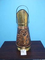 Front view of the tall brass jug with handle, showing embossed musical figure.