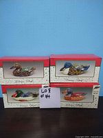Photo of all 4 ceramic duck figurines in their original boxes showing the front and top with red lids