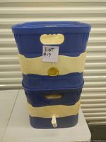 Front side view of stacked two blue and white water containers, lower container has white spigot visible