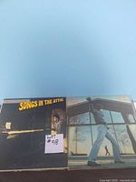 Photo showing two album covers in the record lot, one titled 'Songs in the Attic' and the other featuring a man outside a building.