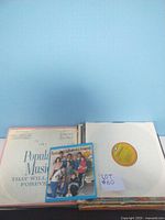 Photo showing several vinyl records stacked, including "Popular Music That Will Live Forever" and a small colorful disc labeled "Kool & The Gang McDonald's House".