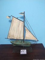 Front view of metal sailboat decorative model with white sails and green hull on black base.