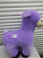Side profile of purple llama plush showing its rounded body, tail, and black feet.