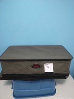 Closed gray rectangular golf bag organizer with SKB logo on front, placed against a light blue wall.