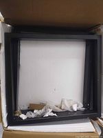 Box containing two black steel tube table legs with assembly hardware inside.