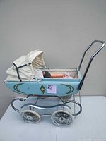Side view of the vintage blue toy doll stroller showing the dented side, canopy in good condition and one doll inside