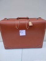Front view of vintage brown leather suitcase with attached luggage tag and white stitching.