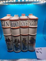 Four vintage ceramic whiskey flasks labeled Gin, Brandy, Rye, and Scotch standing together showing front labels and artwork
