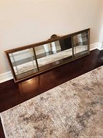 Front view of the full antique horizontal mirror showing the three segmented mirrored panels and wooden frame resting against the wall on a wooden floor.