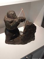 Front-left angle view of Inuit hunter carving aiming bow behind rock.