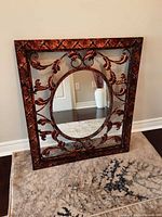 Full view of the oval mirror showing the decorative metal frame with scroll and leaf patterns and diamond textured border