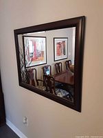 Wall mirror hung on a beige wall showing reflection of a dining room.