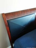 Close-up of headboard showing ribbed carved wood crest rail and black leather padded insert with diagonal stitching