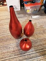 Three red ceramic vases on carpeted floor showing size and shapes.