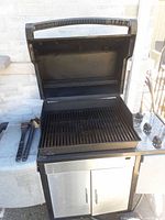 Grill open showing cooking grate and two grilling tools on left side table