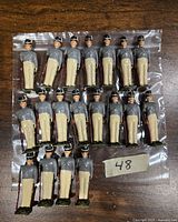 Displays 19 painted metal Britains miniature soldier figures arranged in rows in a small plastic bag on a wooden surface.