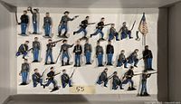 Top view of 27 painted lead miniature U.S. Civil War soldier figures laid out in tray, including flag bearer and figures wielding rifles and pistols.