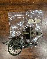 Two green painted functional artillery miniatures with match firing capability, on a wooden surface inside plastic bag.