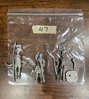 Three unassembled metal miniature military figures in a clear plastic bag, labeled with number 47, showing detailed miniature parts including weapons and bases.