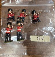 Five painted lead miniatures of Britain's Royal Guard soldiers in various shooting poses, shown inside clear plastic bag on wooden tabletop, tagged with the number 54.