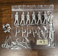 Six unpainted vintage Britains lead soldiers in standing position, arranged in a plastic bag. Also visible are 12 spare arms, 8 spare heads, and 2 lead standard banners all unpainted and silver colored.