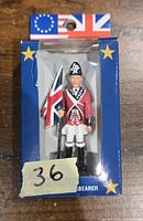 Photo of unopened British flagbearer figurine in blue box with stars and flags on top showing figure holding British flag.