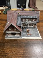 Close-up photo of painted 1/87 scale bakery and monument building with stone paved courtyard, miniature figures on roof and patio.