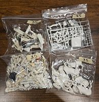 Four clear plastic bags containing assorted 54mm Historex and Airfix miniature parts including infantry figures, unassembled sprues, and horse figures laid out on wooden surface.