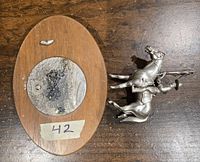 Photo showing metal Canadian Mountie figure with broken horse legs placed next to an oval wooden base with adhesive residue on top.