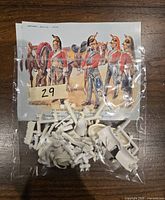 Plastic unassembled miniature parts in a clear bag with a printed colored reference sheet showing the completed figures and soldiers in historical red uniforms with cavalry helmets and horses.