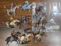 Photo showing nine metal miniature riders on horses in various action poses, painted in multi colors including traditional Native American attire and Western cowboy outfits.