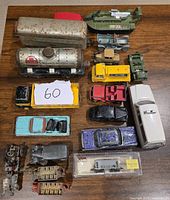 Top-down image of a collection of vintage painted metal vehicle toys on a wooden surface, including cars, trucks, military vehicles, trains, and a hovercraft toy.