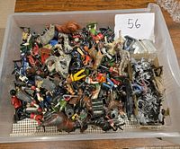 Plastic container filled with assorted vintage Britains lead miniatures and other vintage metal miniatures including painted lead soldiers, horses, and unpainted metal figures showing varied wear and condition.