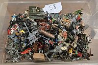 Photo showing a large variety of vintage Britains lead and metal miniatures, including soldiers, knights, horses, and a small tank model packed in a plastic container.