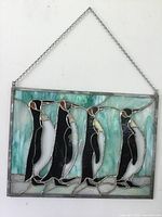 Front view of the stained glass penguin panel hanging by a metal chain against a white background.