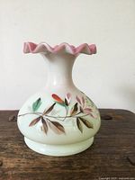 Photo of antique opaline vase showing white glass body with hand painted leaves and flowers and pink ruffled rim.