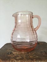 Side view of pink depression glass pitcher showing the ribbed decorative pattern and solid handle.