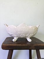 Front side view of pale pink milk glass footed bowl showing scalloped edge and floral texture.