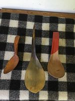 Three antique primitive carved wooden ladle spoons arranged on black and white checkered fabric background.