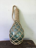 Front view showing light blue pontelled glass ball with rope netting and handle loop.