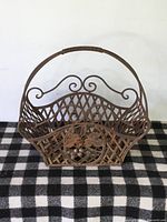 Front view of antique wrought iron basket showing decorative scrollwork, lattice design, and floral motif on front panel.