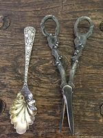 Serving spoon and scissors placed on wooden surface showing detailed ornate designs on both items.