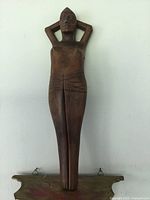Full length front view of antique wood carving of male figure with arms behind head, mounted on a wall bracket.